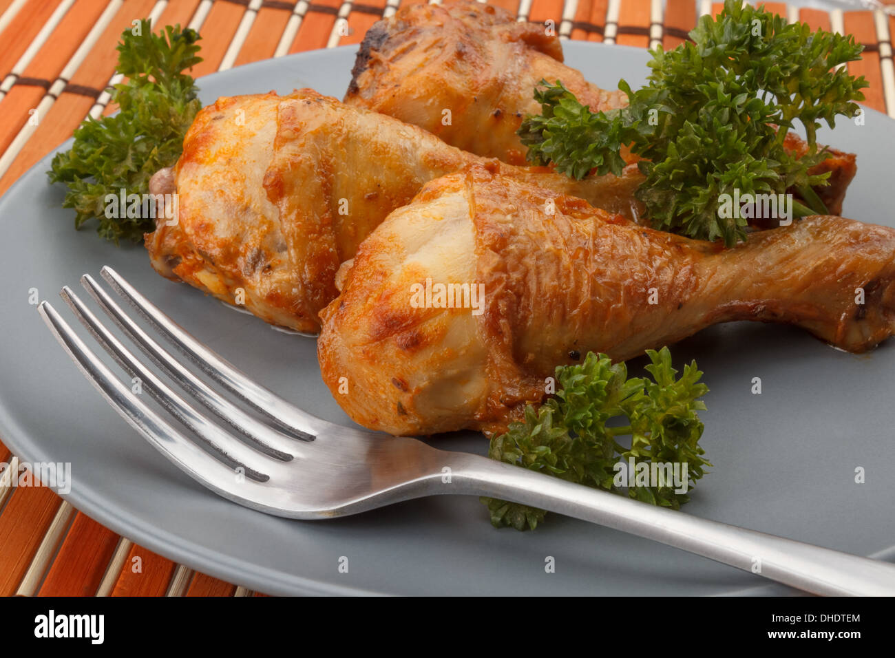grilled chicken legs served with parsley sitting on a gray plate next to a fork Stock Photo