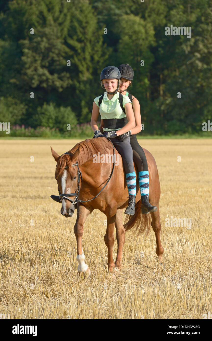 Two girls (wearing helmet and back protector) riding together on back