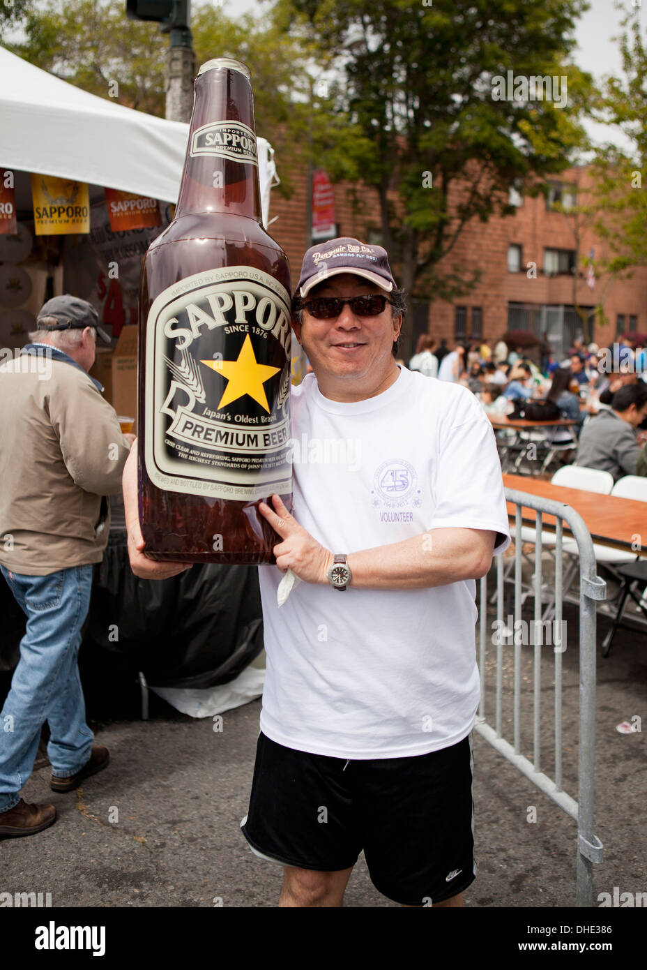 Japanese-American man holding large blowup Sapporo beer bottle at festival - San Francisco, California USA Stock Photo