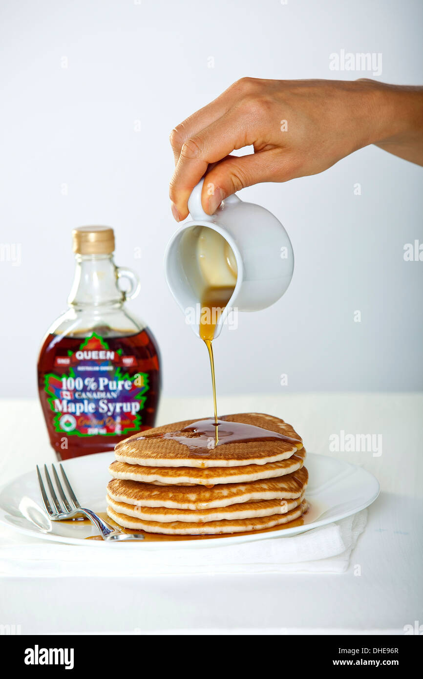 A hand pouring maple syrup from a jug onto a stack of pancakes. Stock Photo