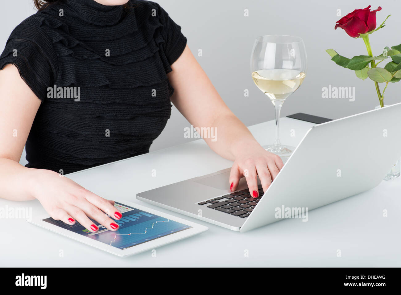 A business woman is working with the modern laptop and tablet computer. Nearby on the table is a glass of wine and one rose. Stock Photo