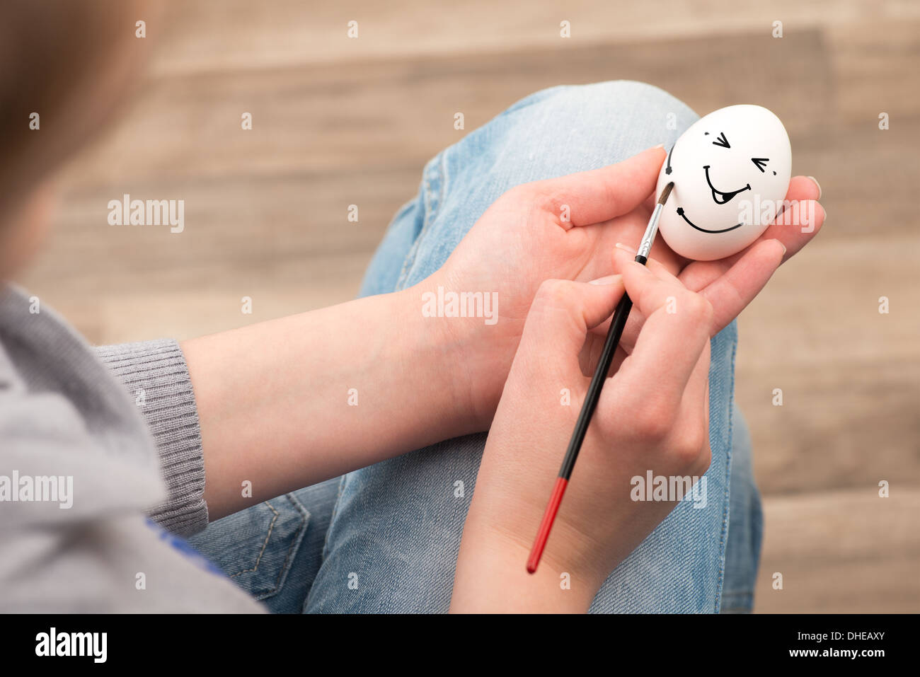 The girl draws with a brush on an white egg. Egg laughs. Stock Photo