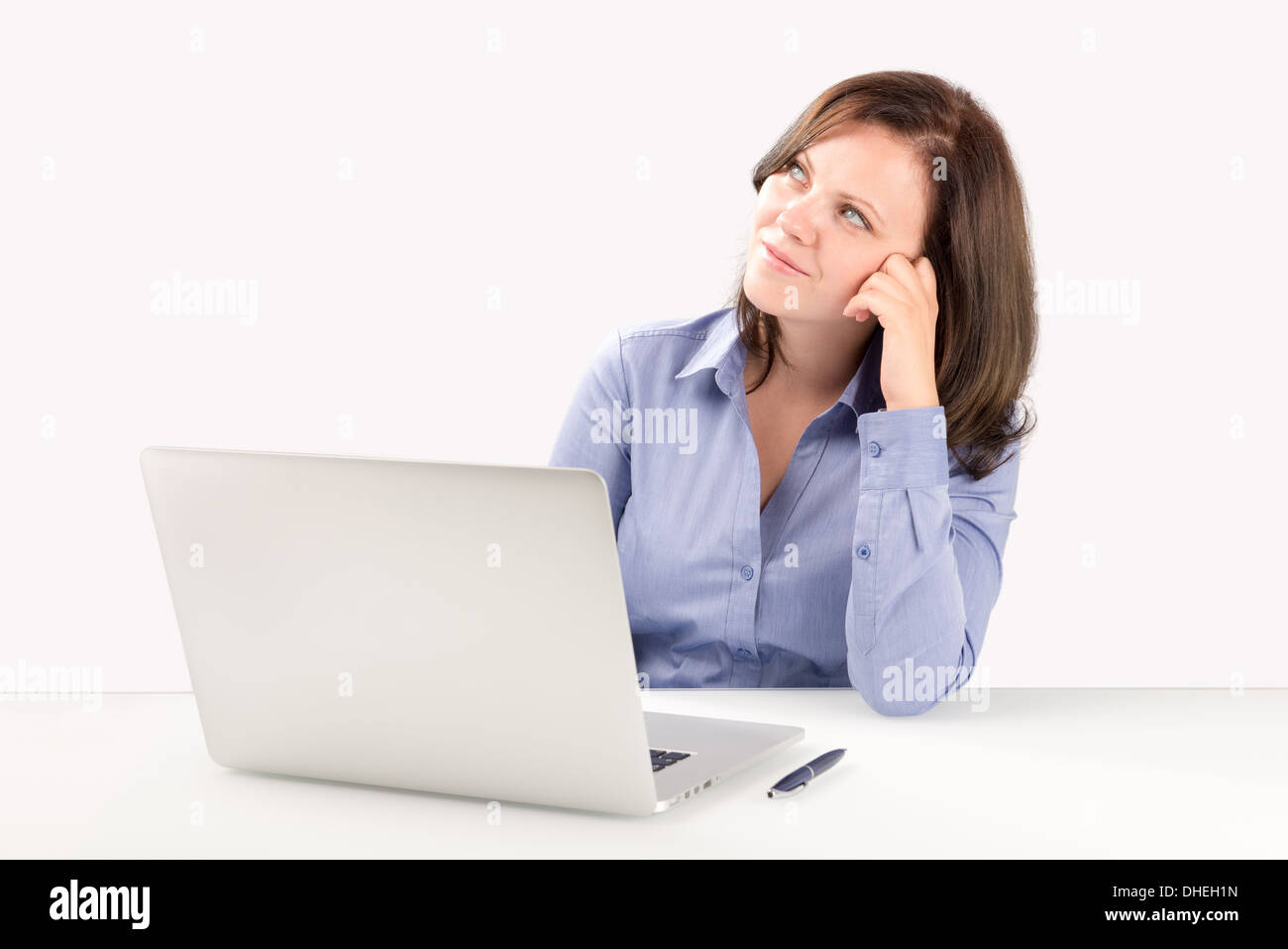 Business woman is sitting in front of a laptop leaning on one arm and looking into the top corner of the screen Stock Photo