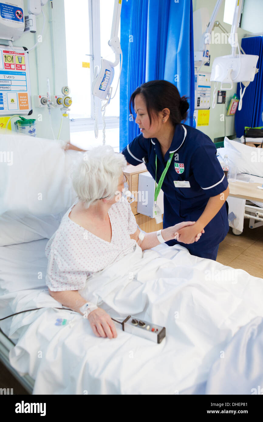 A female Filipino nurse assists an elderly woman in bed UK Stock Photo