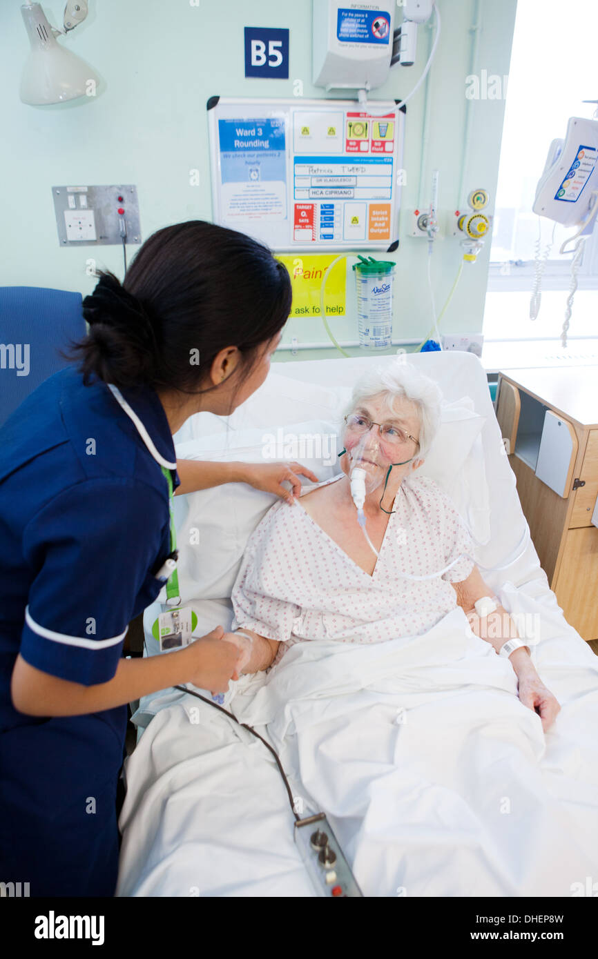 A female Filipino nurse assists an elderly woman in bed UK Stock Photo