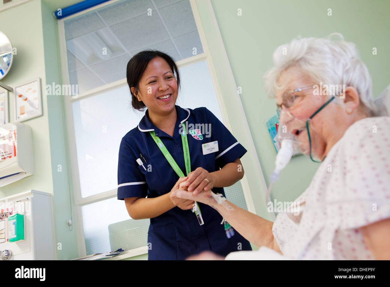 A female Filipino nurse assists an elderly woman in bed UK Stock Photo