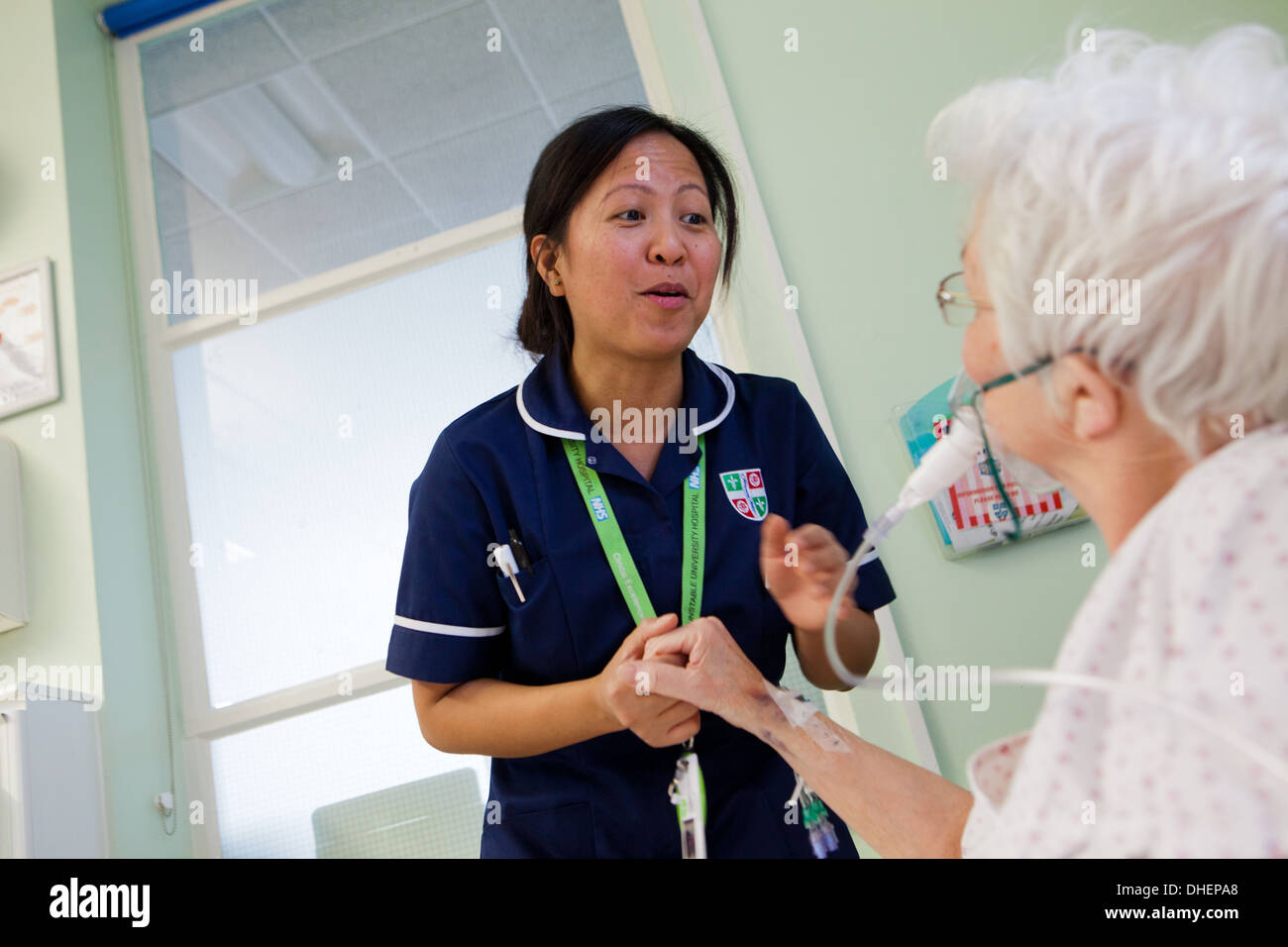 A female Filipino nurse assists an elderly woman in bed UK Stock Photo