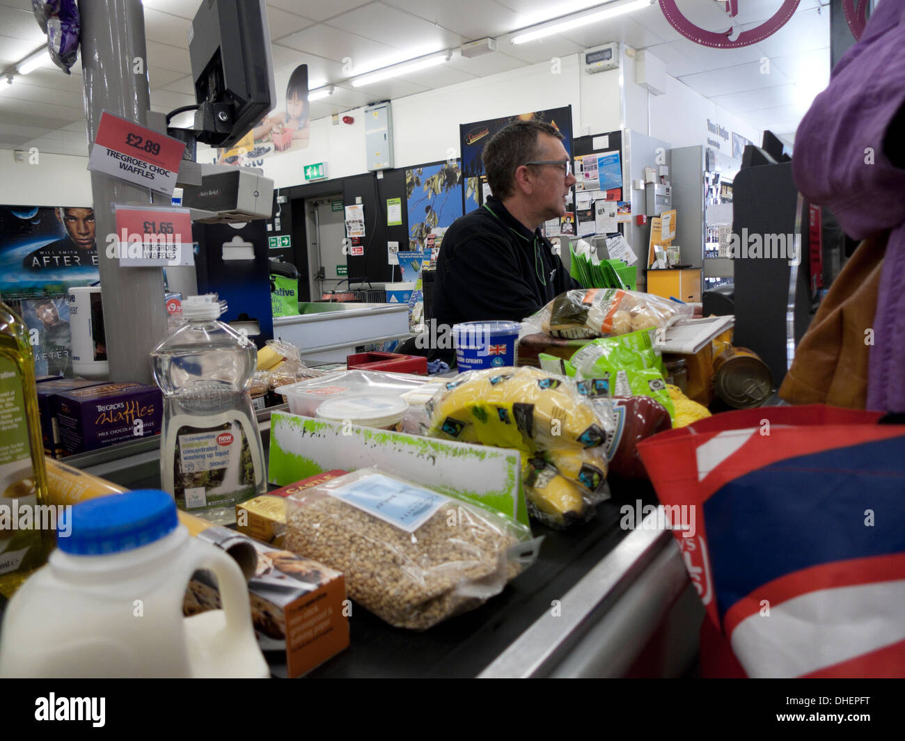 A male worker employee working at the checkout counter filled with groceries food milk plastic packaging in Co-Op supermarket Wales UK KATHY DEWITT Stock Photo