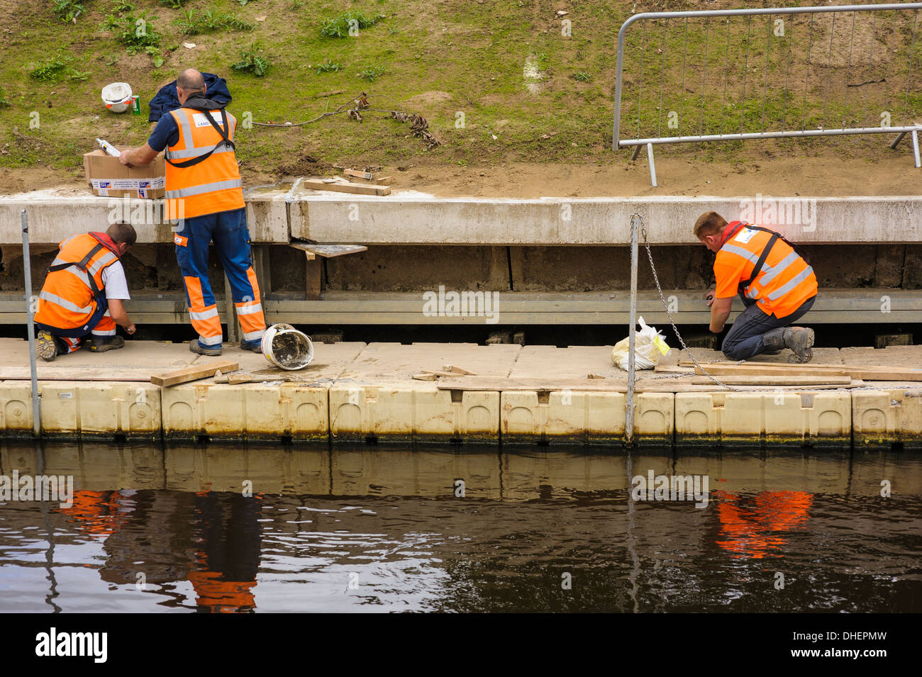 Three workmen repairing a riverbank defense defence defenses defences on the River Ouse. Stock Photo