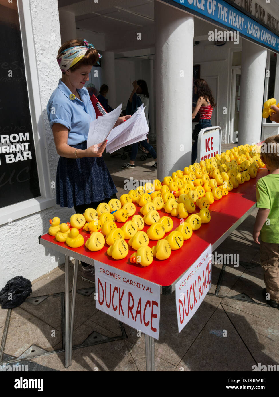 Woman stood behind table full of small yellow plastic ducks for duck race off Cromer Pier Norfolk England Stock Photo