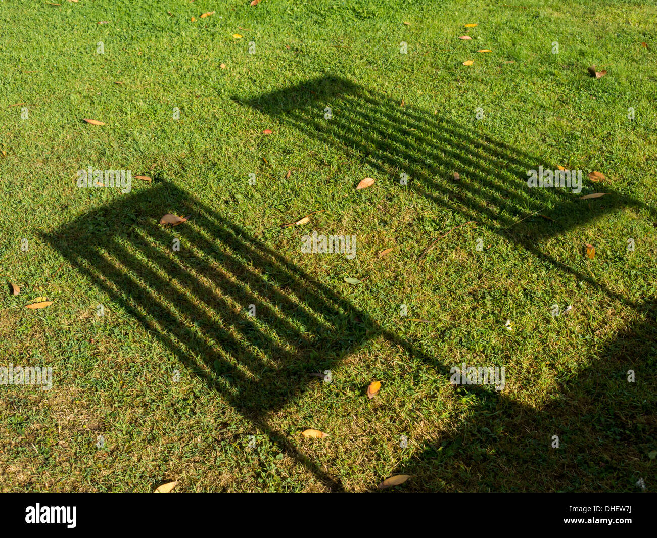 shadows of garden chairs backs cast by the sun falling on grass floor England Stock Photo