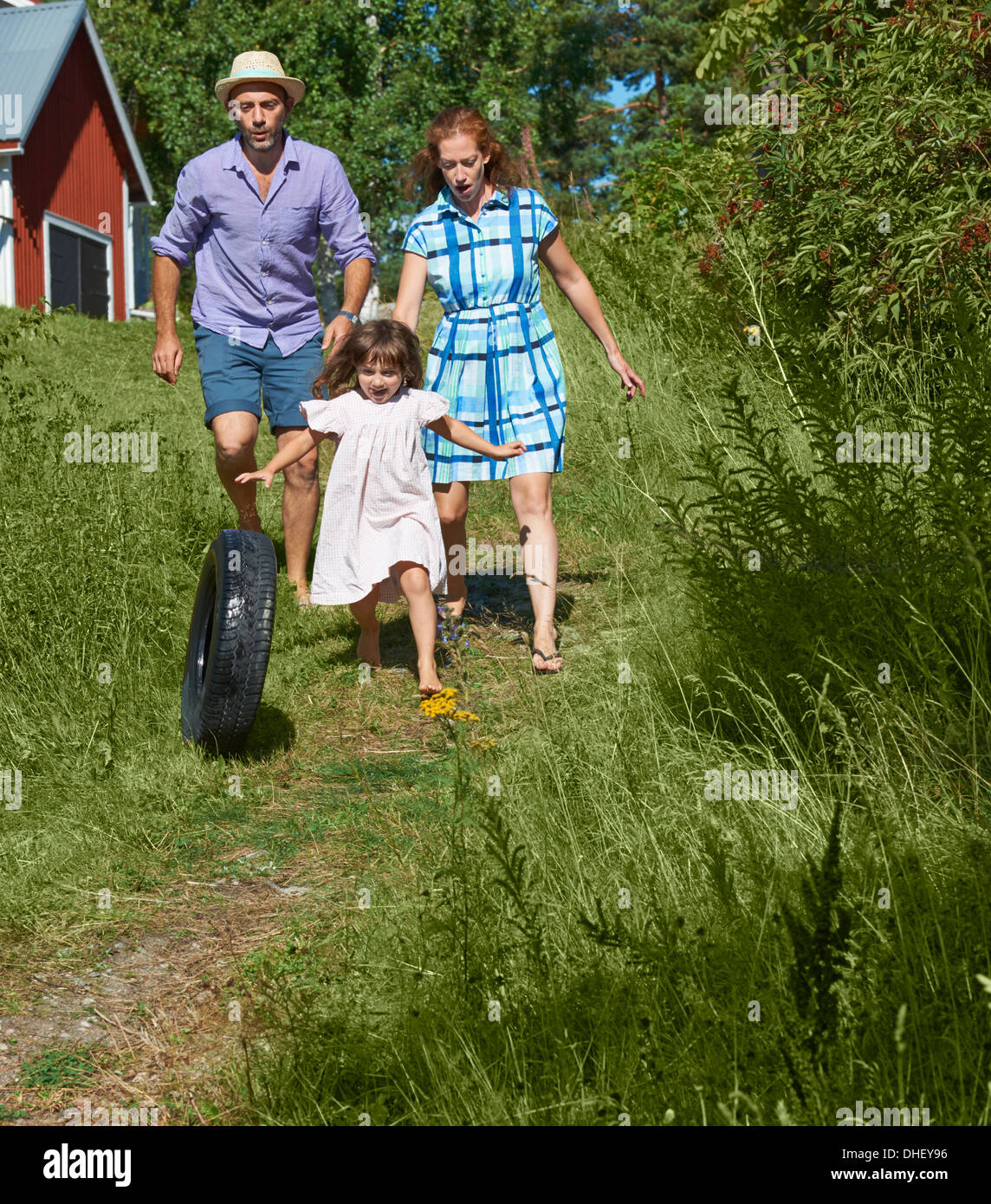 Parents and girl rolling tyre on path, Utvalnas, Gavle, Sweden Stock Photo