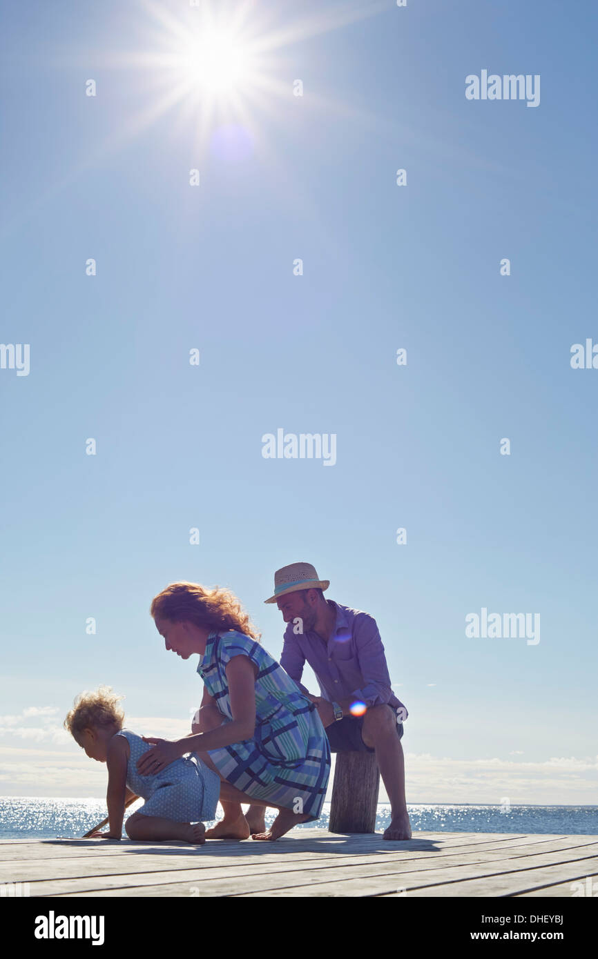 Female toddler and parents kneeling on pier, Utvalnas, Gavle, Sweden Stock Photo