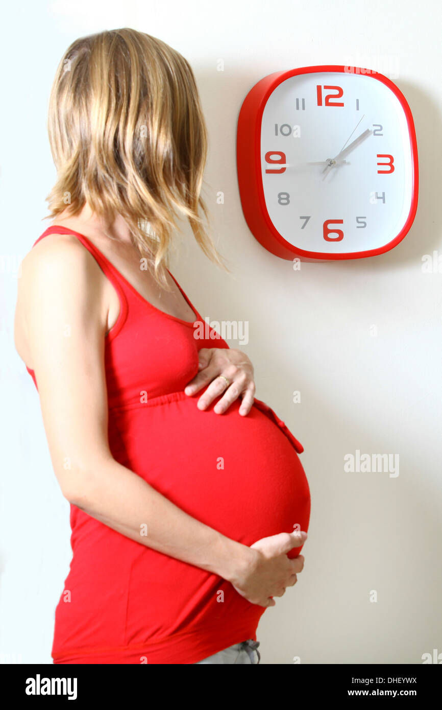 Pregnant woman clock watching in kitchen Stock Photo
