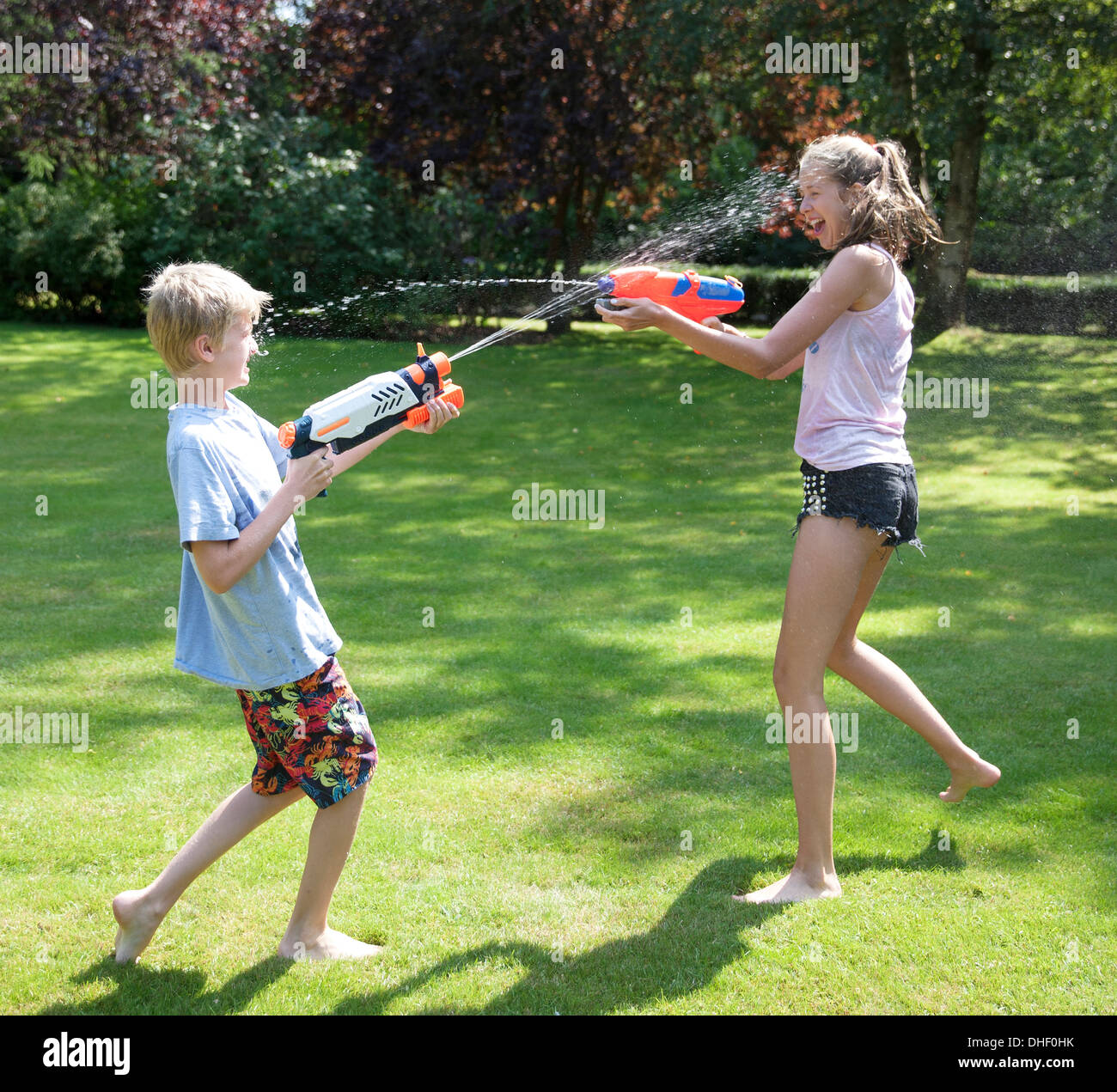 Brother and sister play fighting with water guns in garden Stock Photo