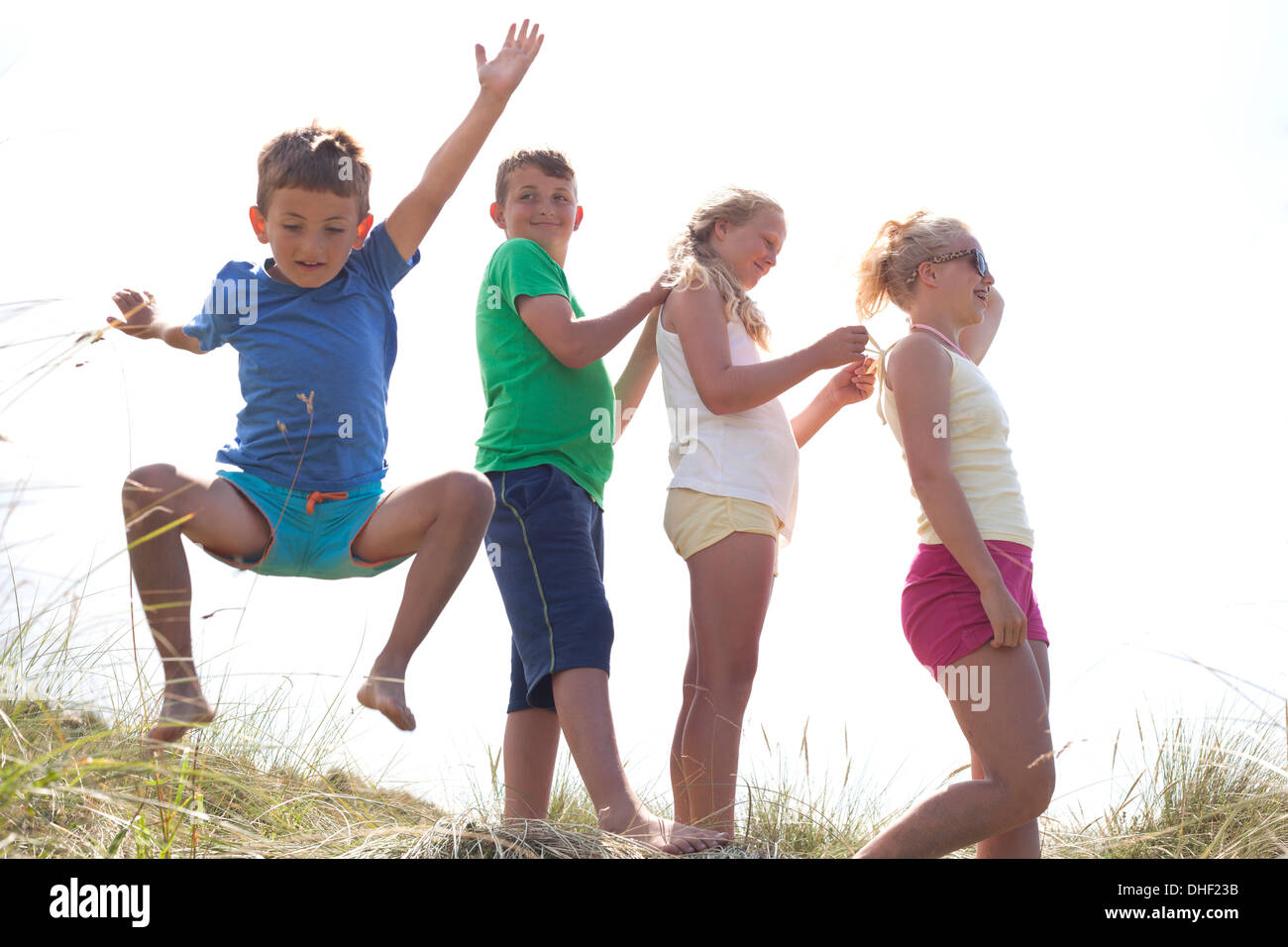 Four friends on dunes, one boy jumping, Wales, UK Stock Photo