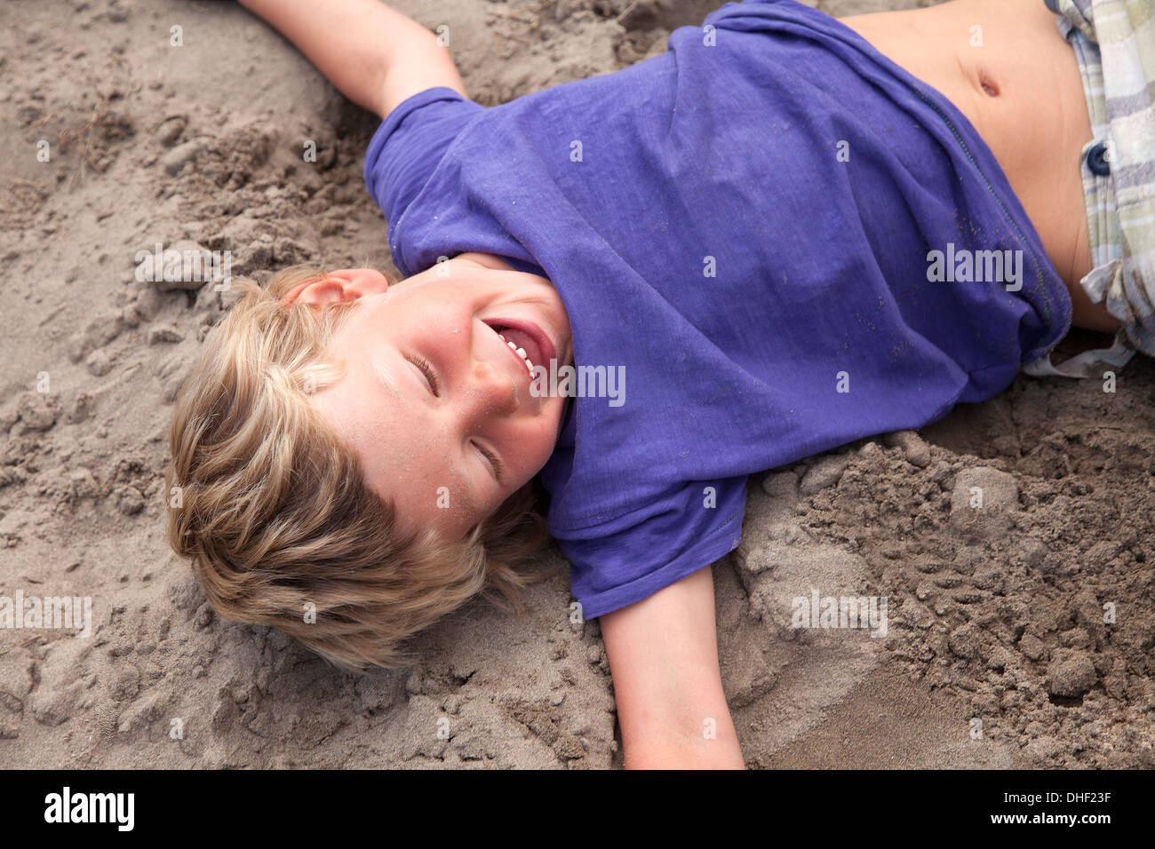 Boy lying on sand laughing, Wales, UK Stock Photo