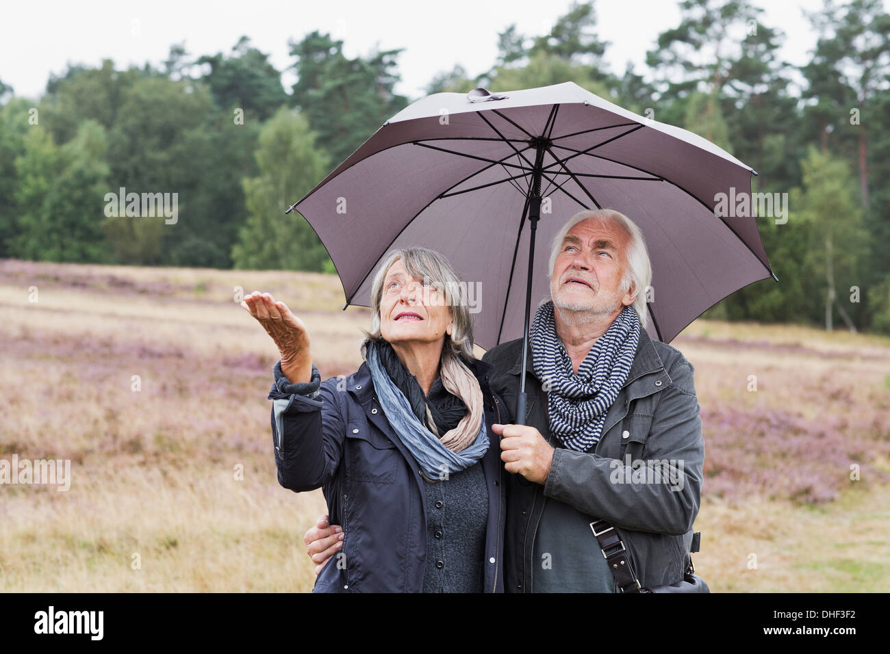 Senior couple under umbrella checking for rain Stock Photo