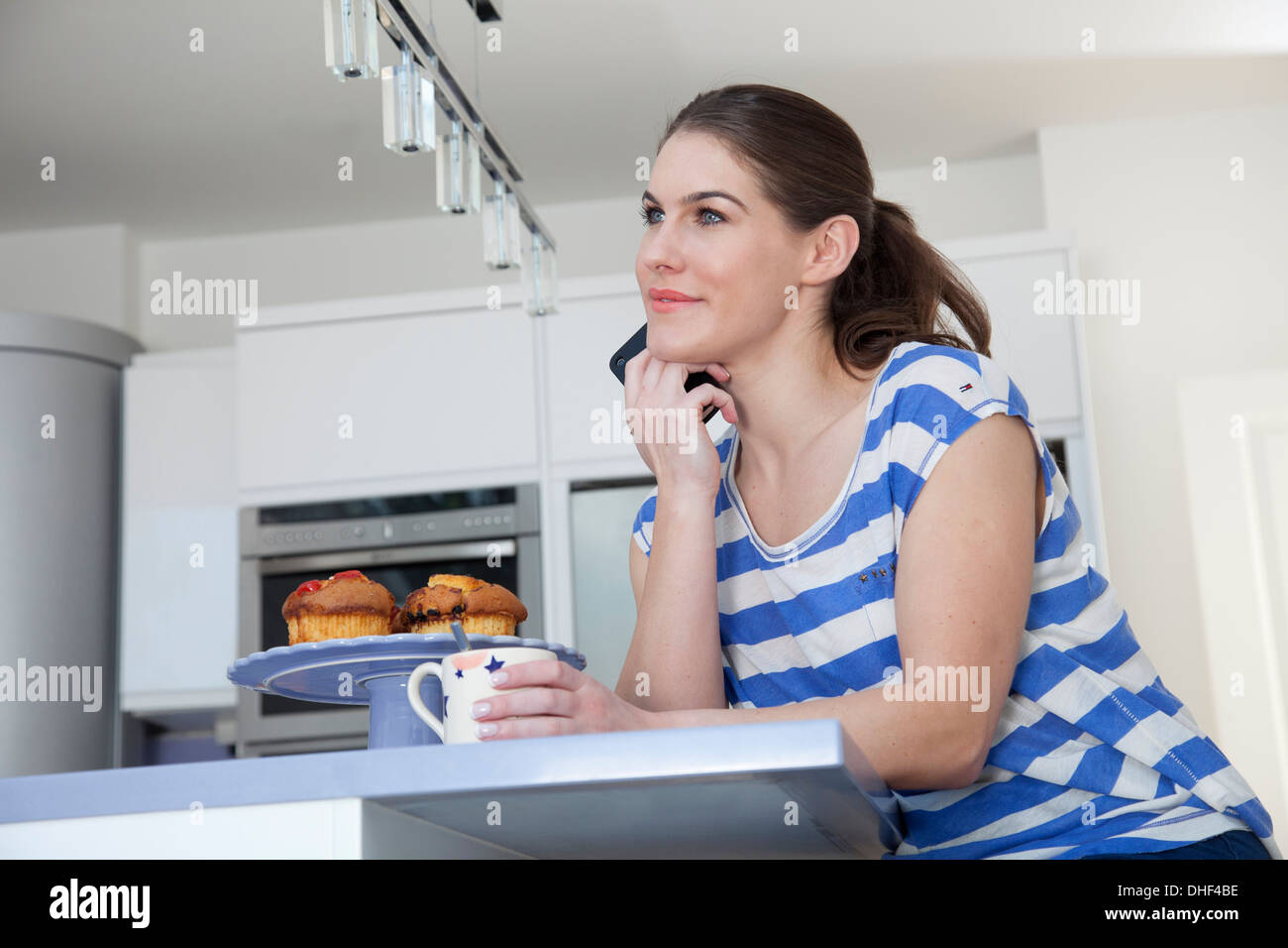 Young woman at breakfast bar with coffee and cell phone Stock Photo