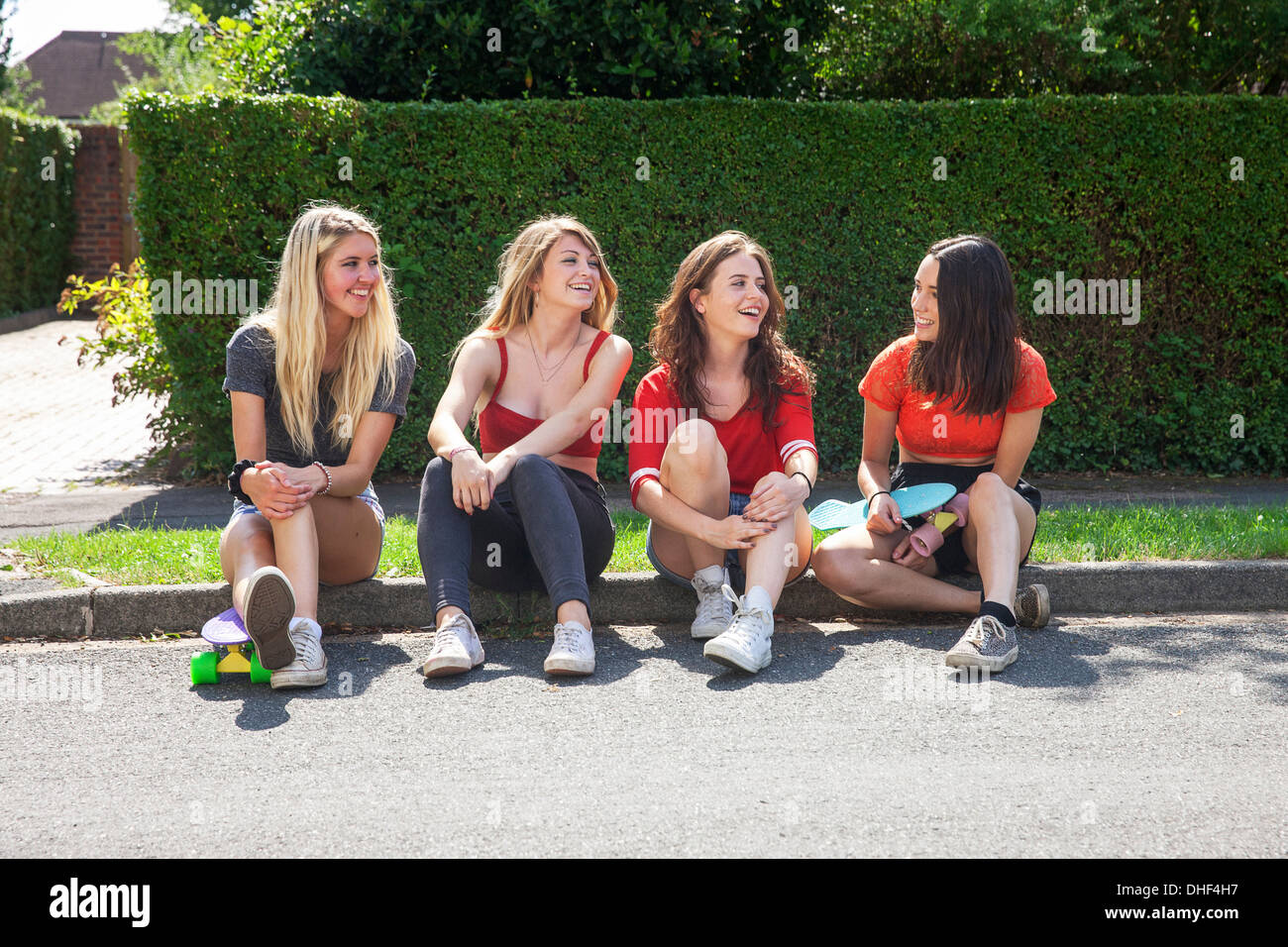 Four young women sitting on kerb with skateboards Stock Photo