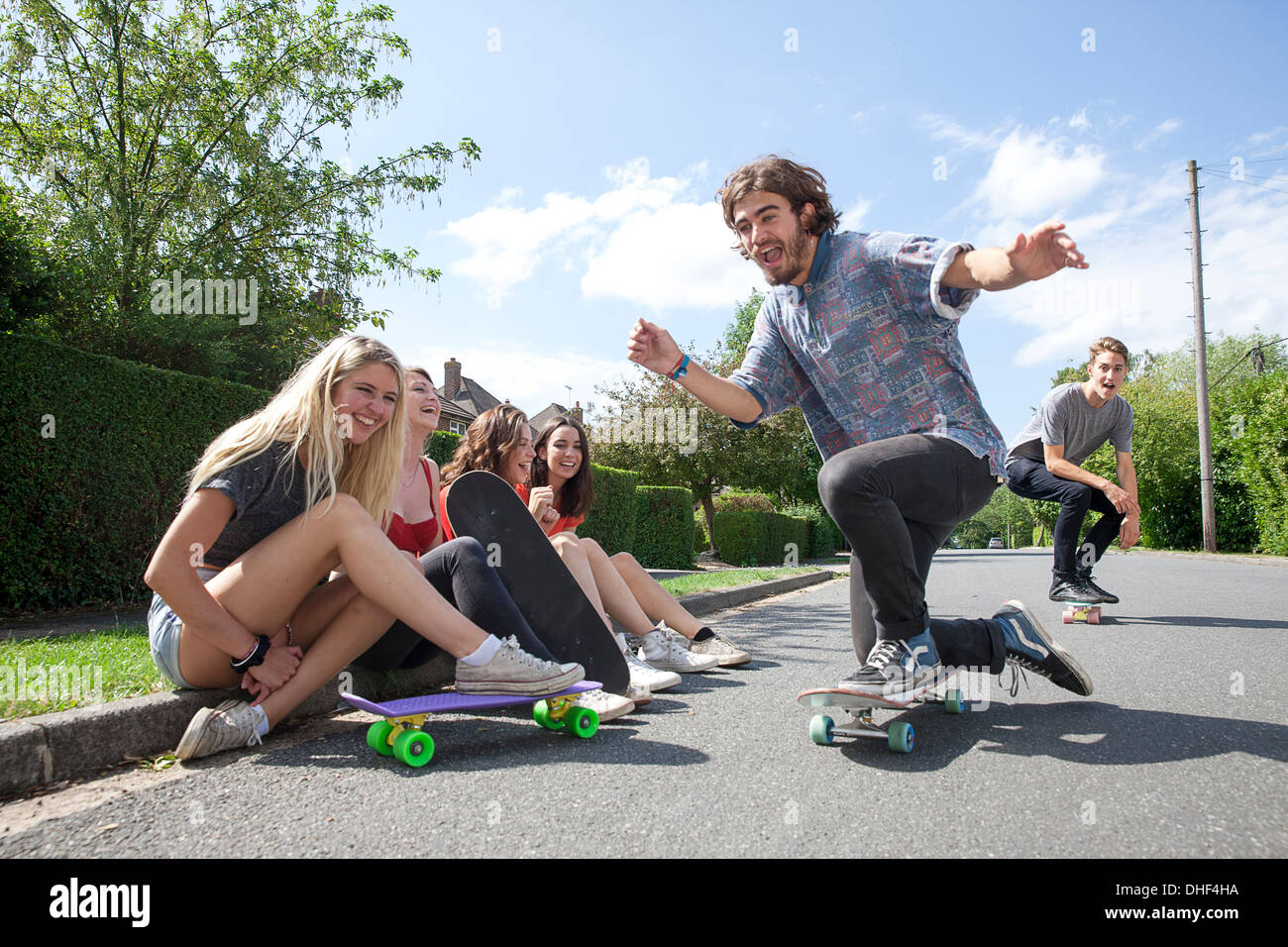 Four young women sitting on kerb watching skateboarders Stock Photo