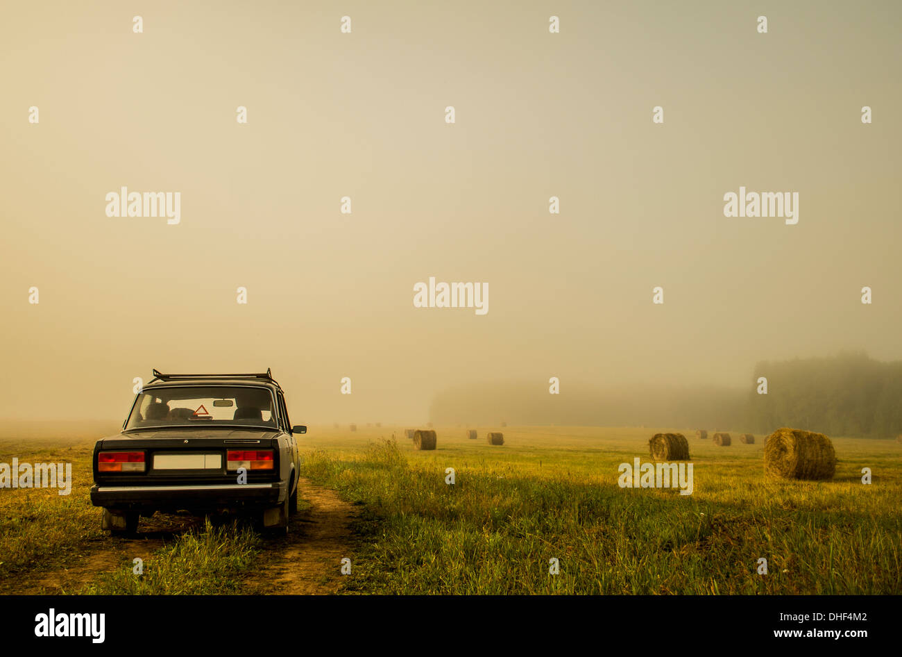 Car driving through field of haystacks on overcast day Stock Photo