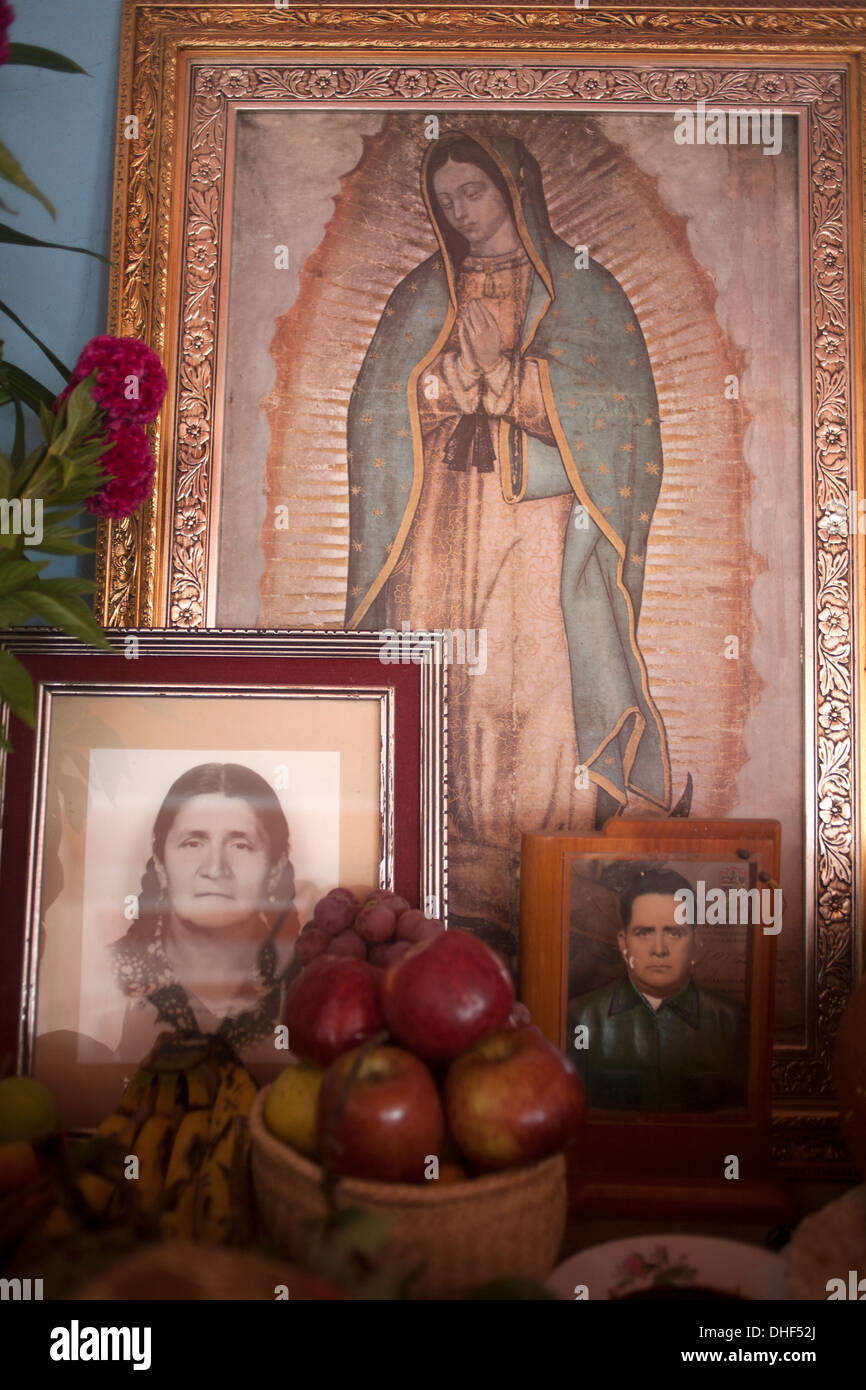 An altar showing an image of Our Lady of Guadalupe, food and family portraits is displayed during Day of the Dead in Oaxaca Stock Photo