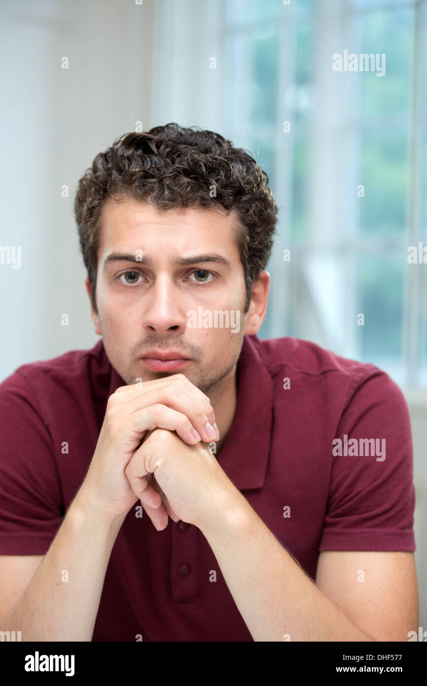 Young man resting chin on clasped hands Stock Photo Alamy