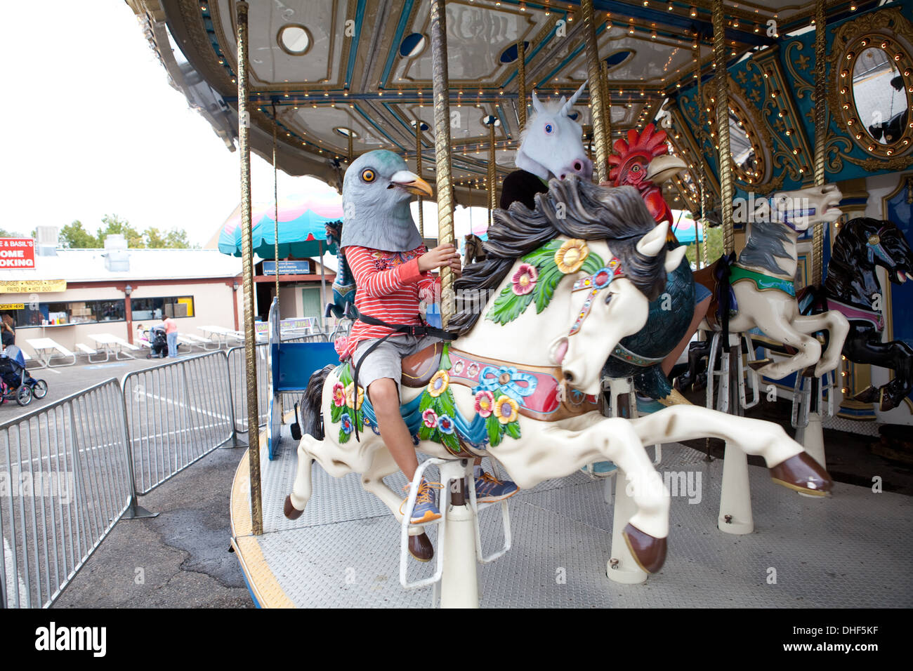 Child wearing a pigeon mask on a carousel, amusement park. Stock Photo