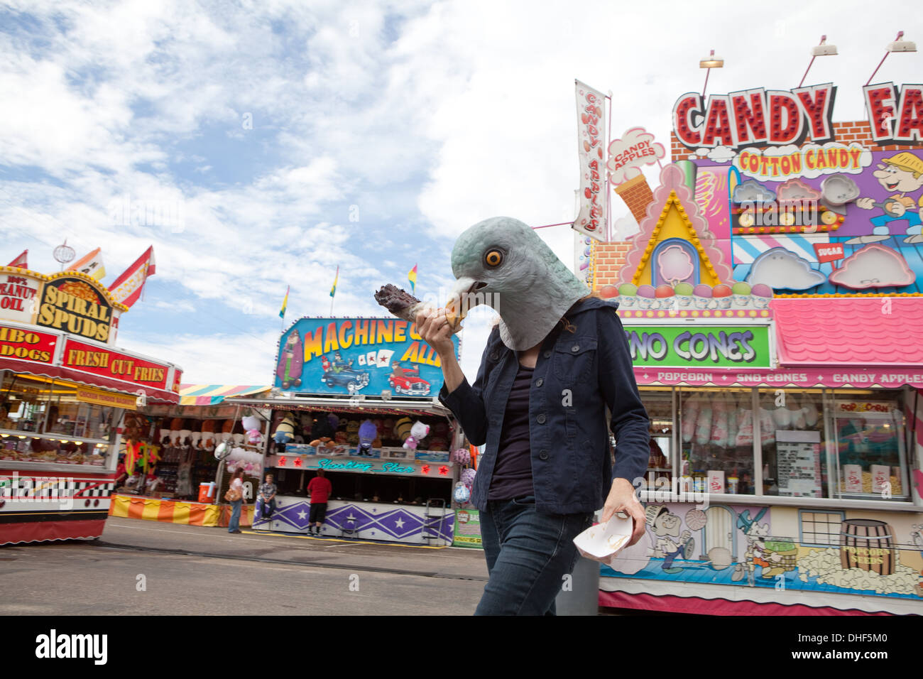woman wearing a pigeon mask stands at a carnival eating a turkey leg. Stock Photo