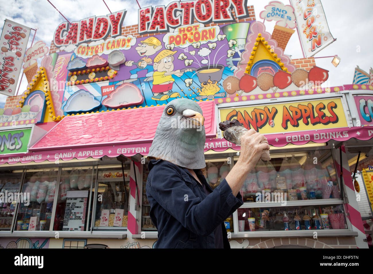 Person wearing a pigeon mask holds a turkey leg at state fair. Stock Photo