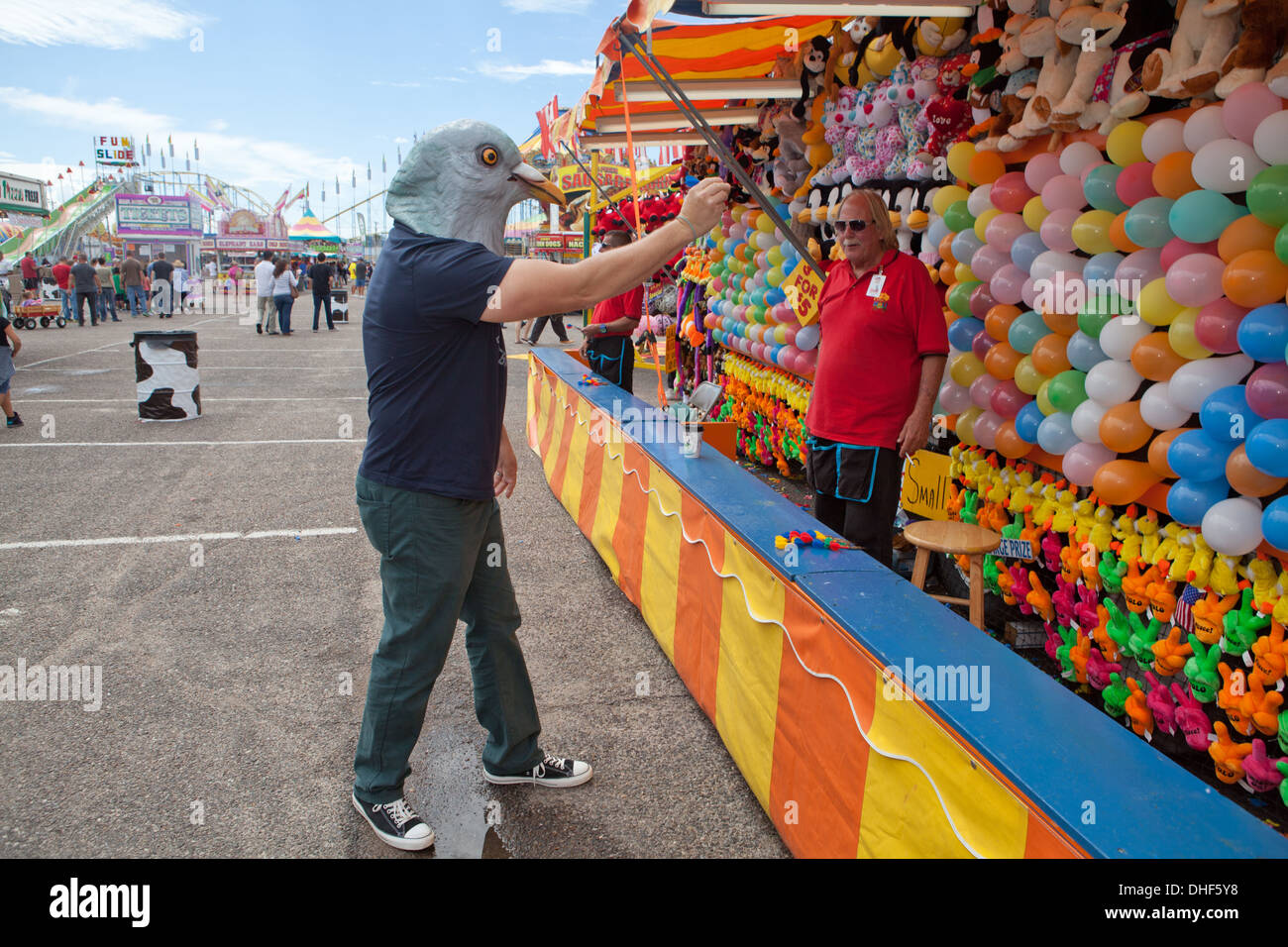 Man wearing pigeon mask aims dart at balloons, New Mexico state fair. Stock Photo