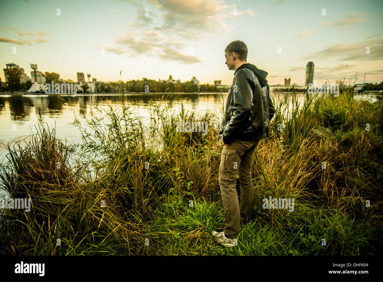 Young man standing on grass looking at water, Russia Stock Photo