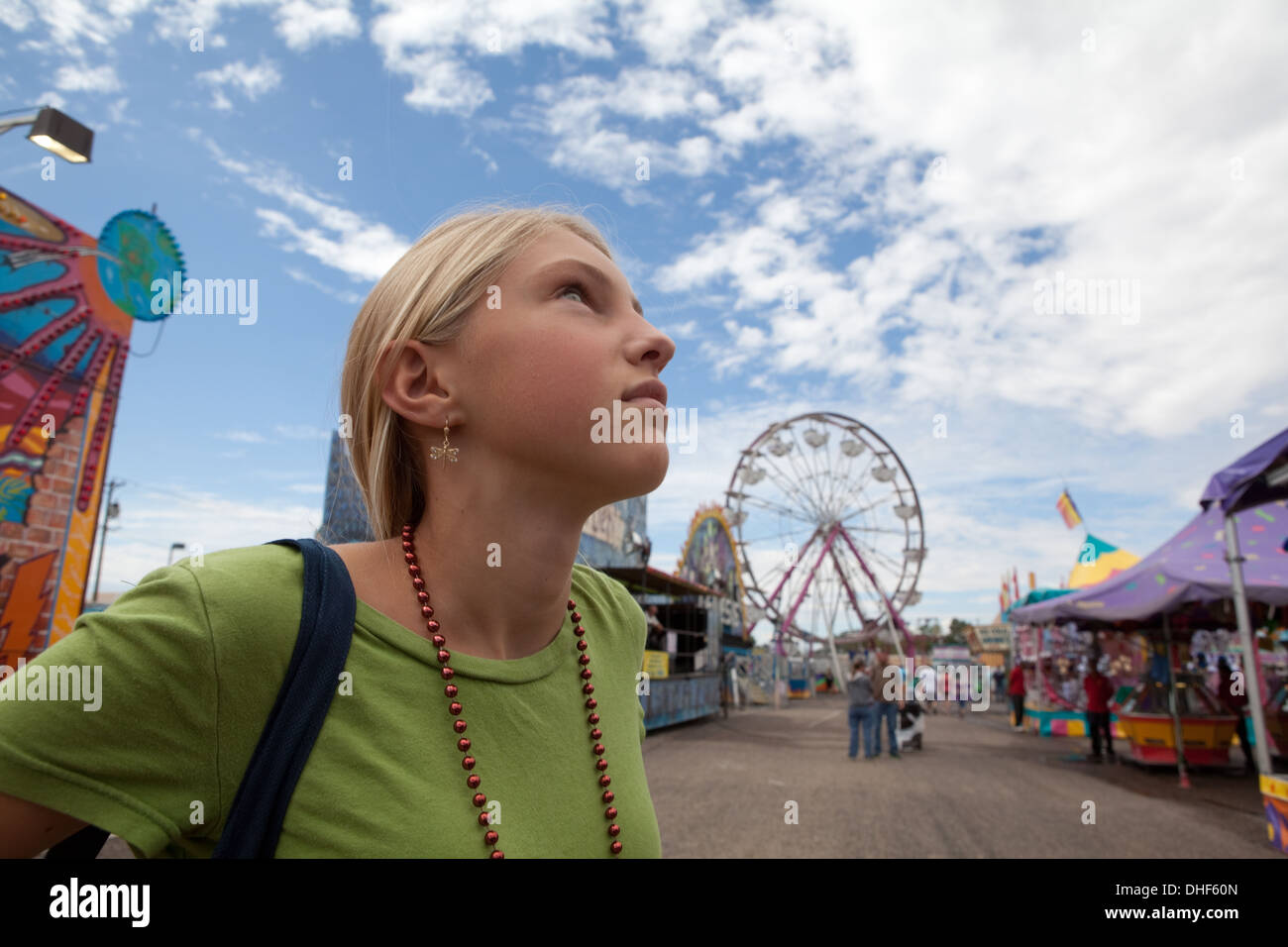Twelve year old girl looks up at amusement park rides with a thoughtful expression. Stock Photo