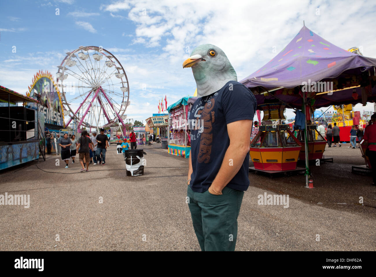 Man wearing a pigeon mask stands at the New Mexico State Fair with ferris wheel in background. Stock Photo