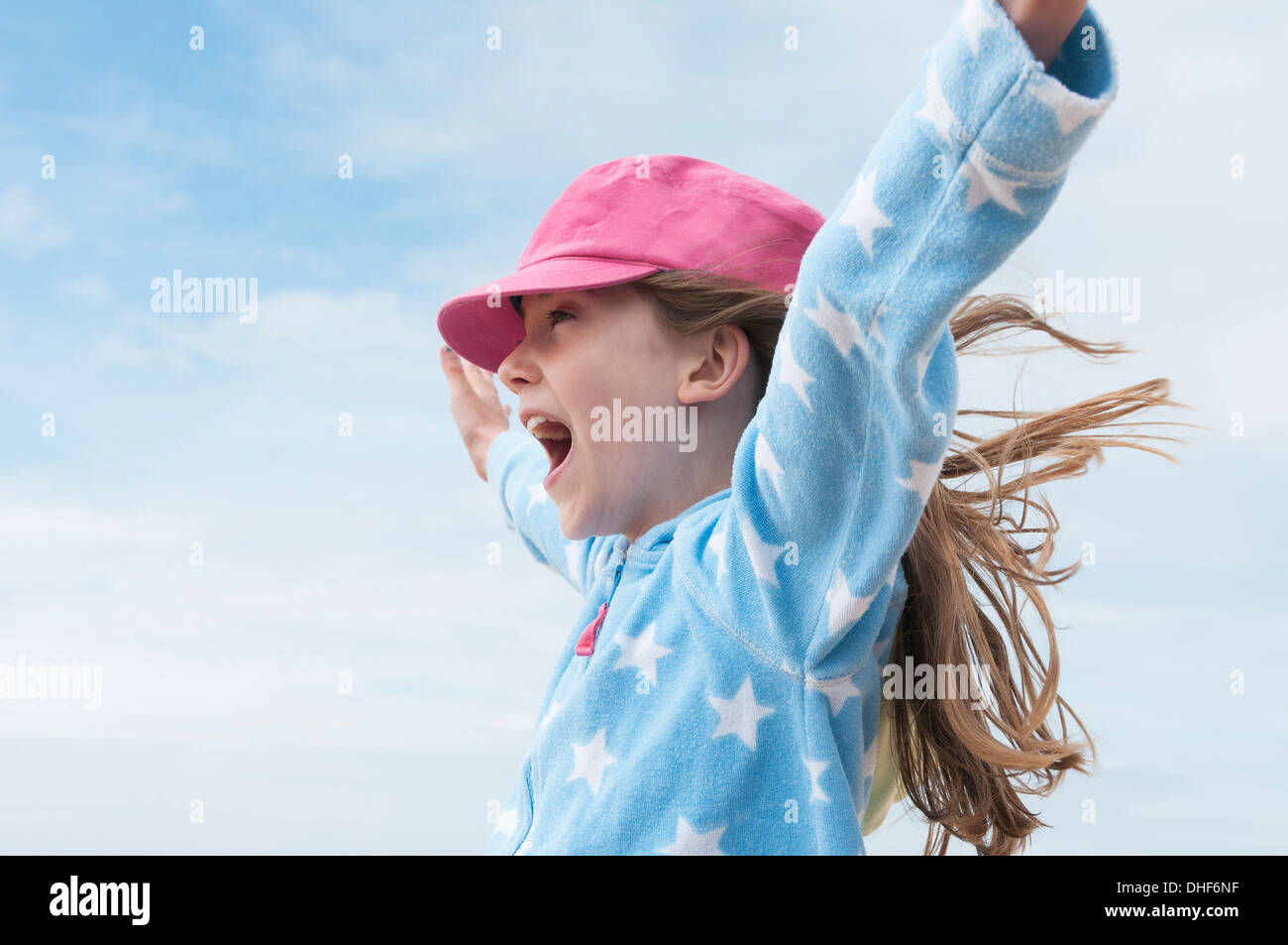 Girl wearing pink cap with arms raised in wind Stock Photo
