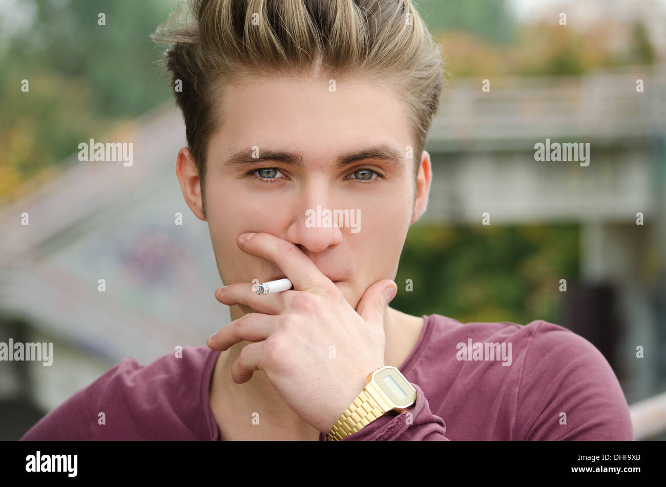 Attractive blue eyed, blond young man smoking cigarette outdoors Stock Photo