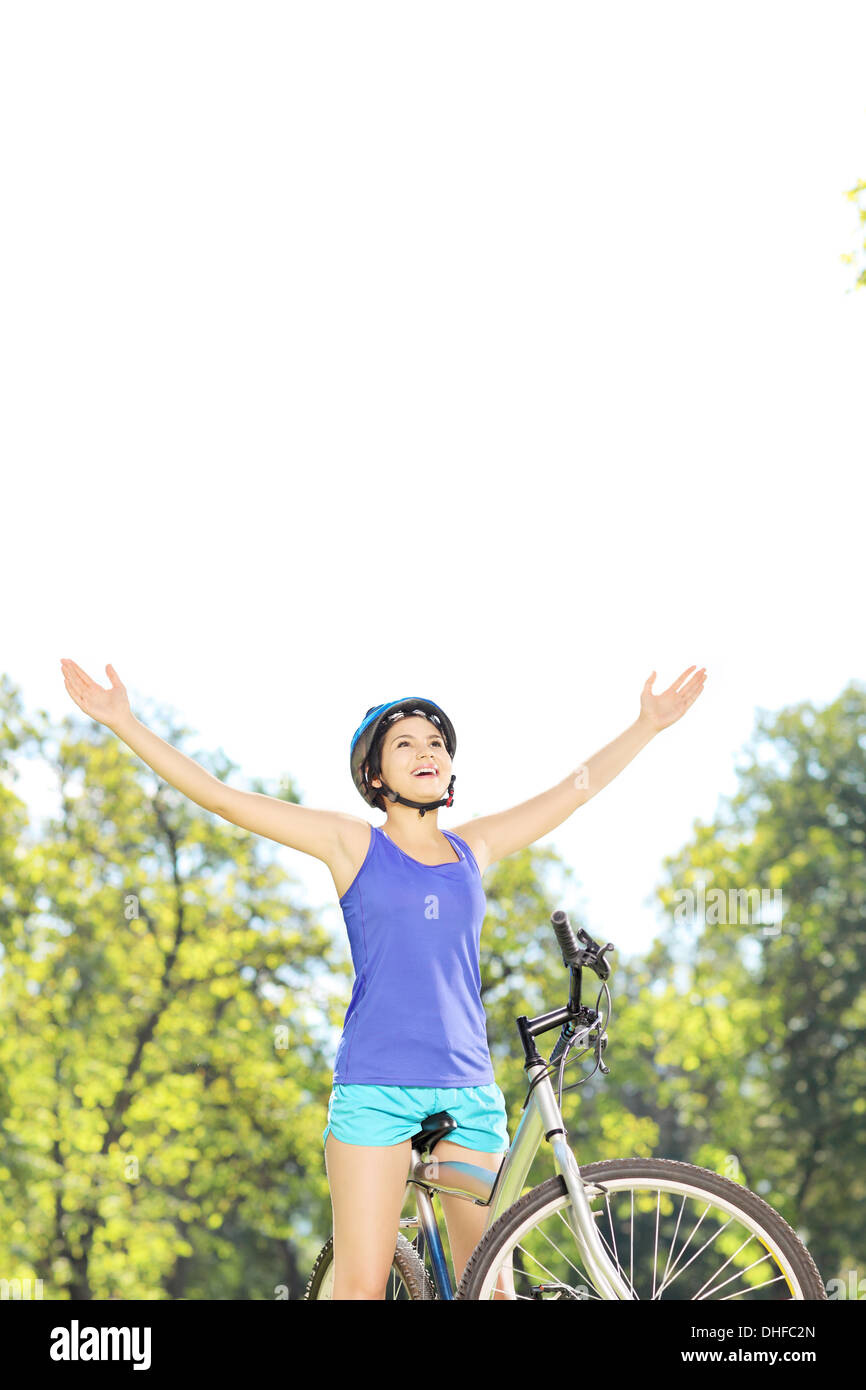 Happy female biker posing with raised hands on a bike in a park Stock Photo