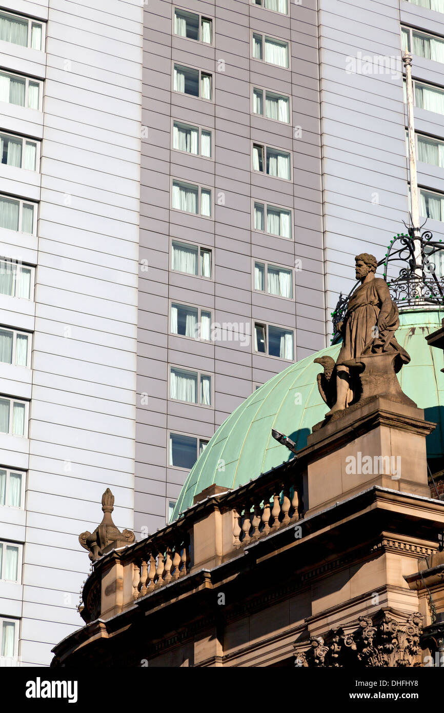 Statue on the roof of a Victorian former bank building with modern apartment block behind. Leeds, West Yorkshire Stock Photo
