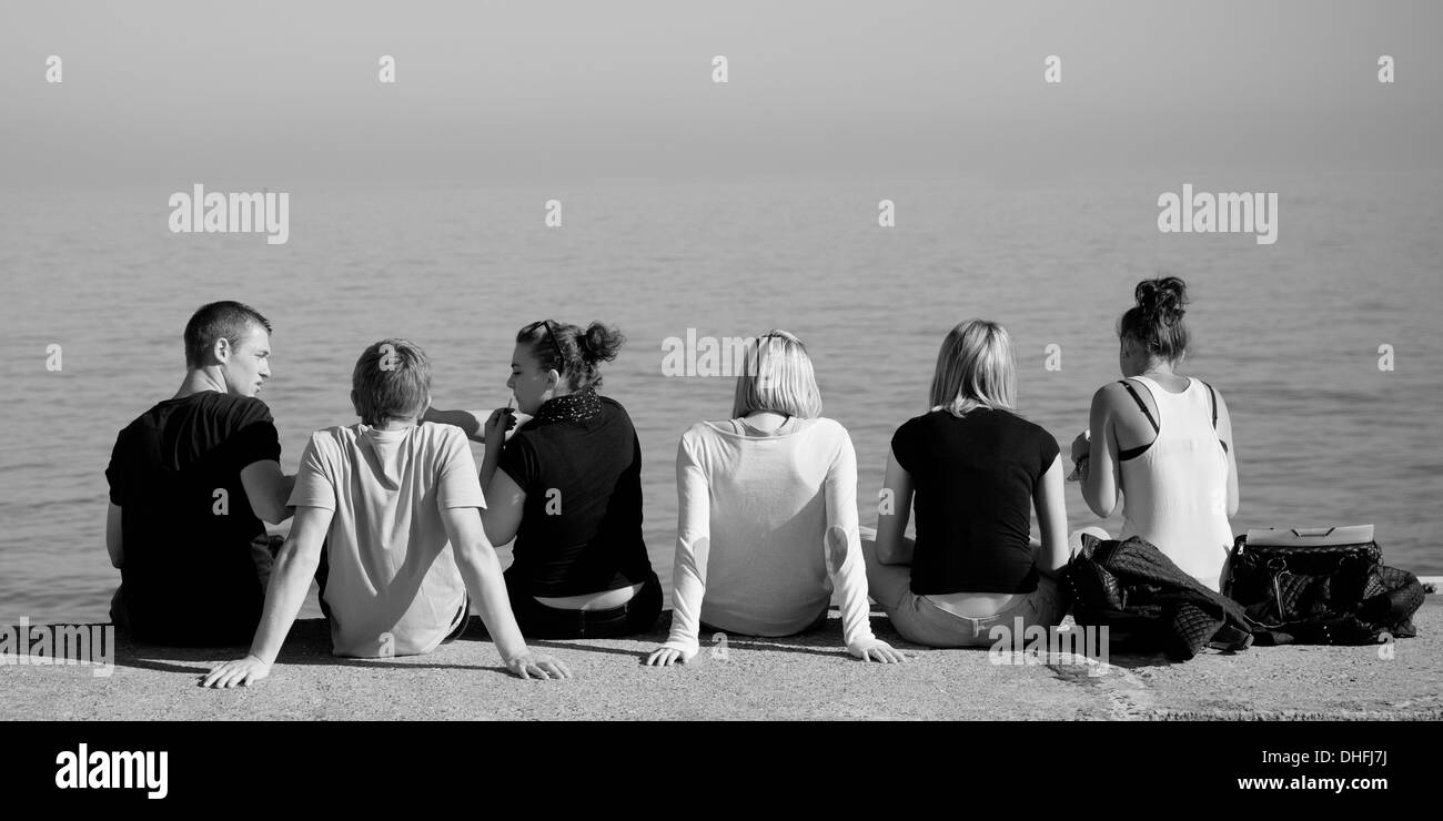 Group of six people sitting on a wall Stock Photo