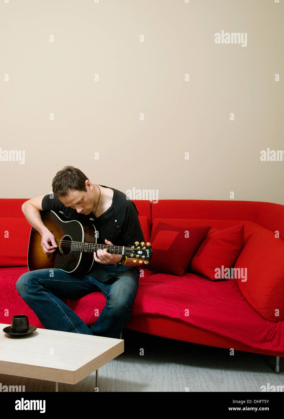 A man sitting on a sofa playing a Gibson guitar Stock Photo