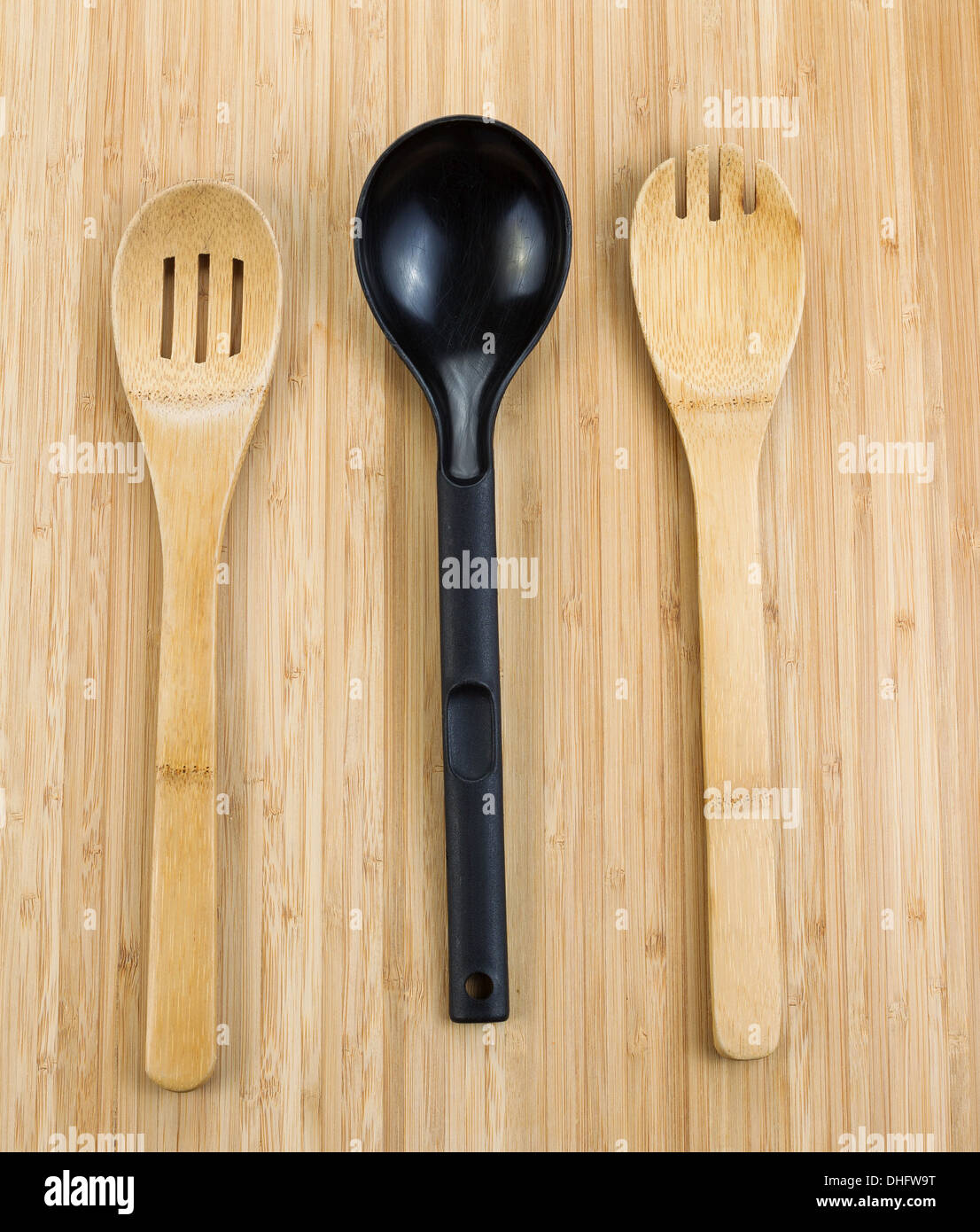 Vertical photo of three kitchen spoons, two of them wooden, on natural bamboo wood Stock Photo