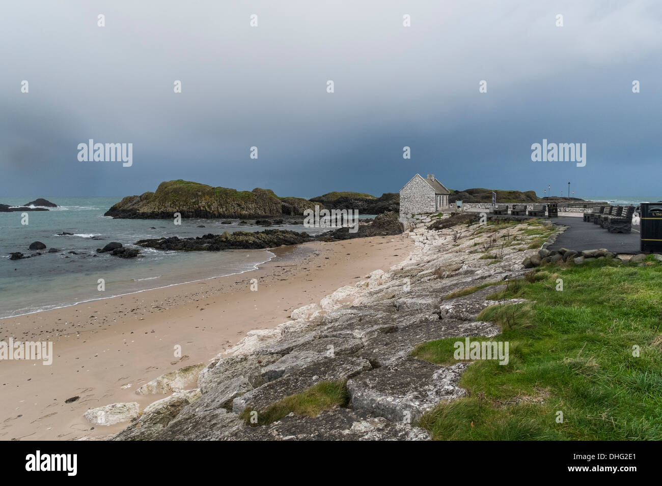 Looking down Ballintoy beach towards the harbour cafe, with a stormy sky developing in the distance. Stock Photo