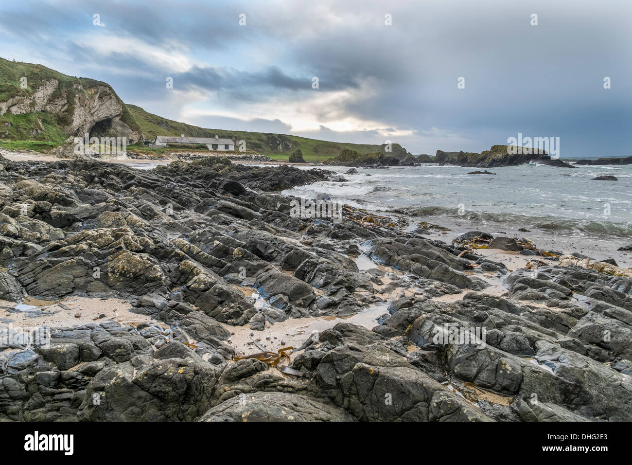 Coastal scene with cottage in the distance, rocky outcrop in the foreground beach. Stock Photo