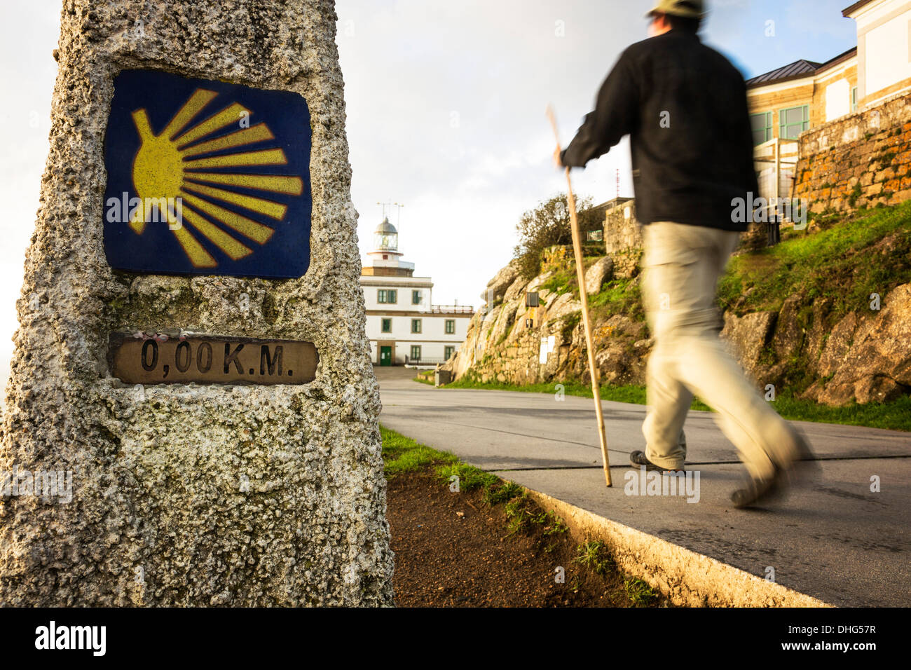 A pilgrim hikes past kilometer zero of the Camino de Santiago towards the lighthouse at Cape Finisterre, Galicia, Spain. Stock Photo