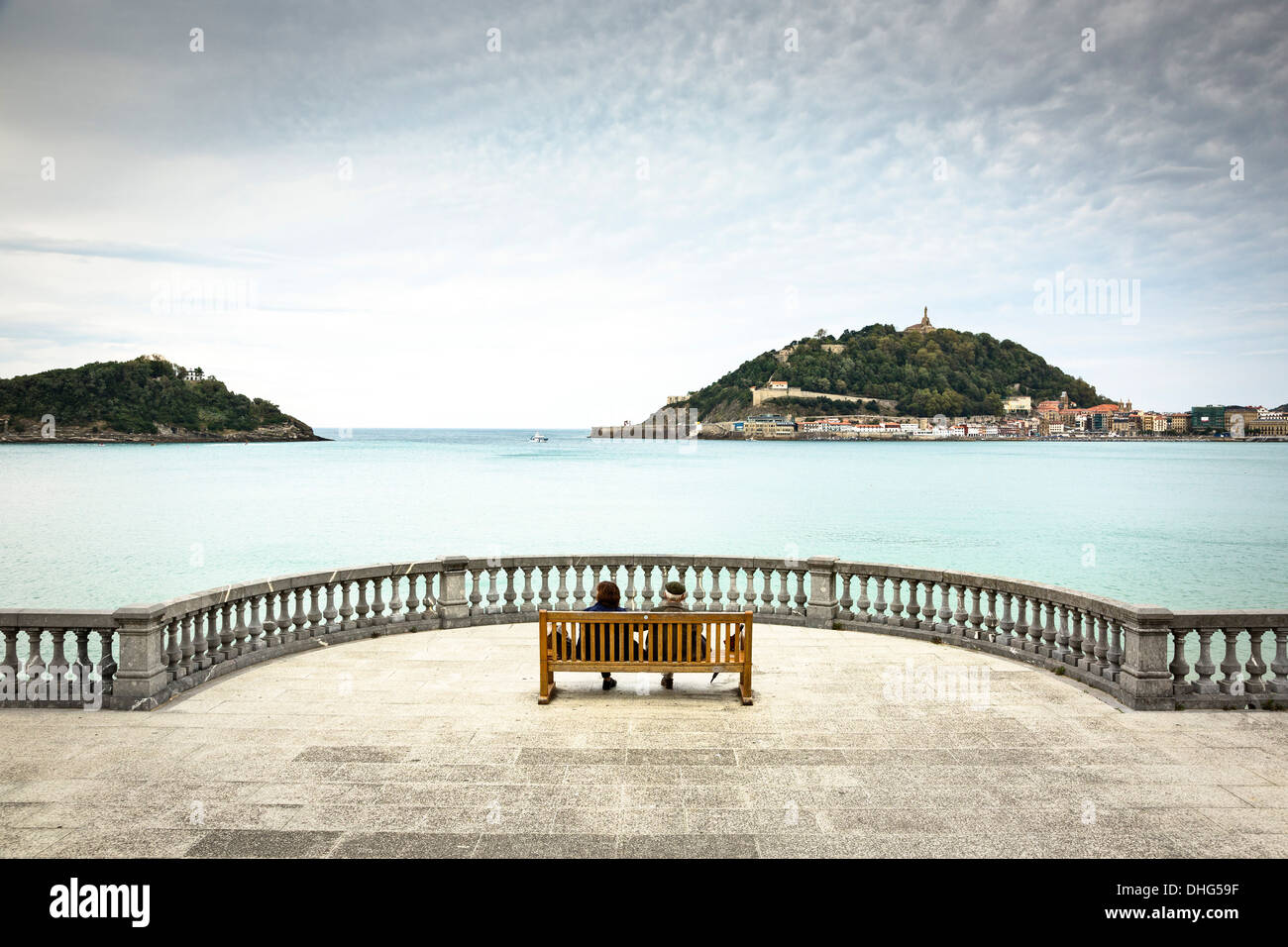 Elderly couple seated on a bench on the boardwalk in San Sebastian, Spain, looking out into the bay. Stock Photo