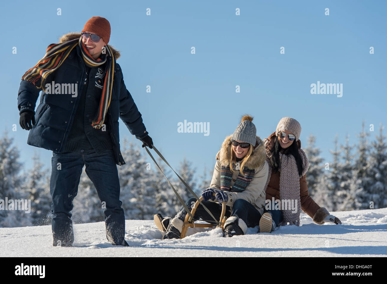 Young people enjoy sunny winter day sledge man pulling girlfriends Stock Photo