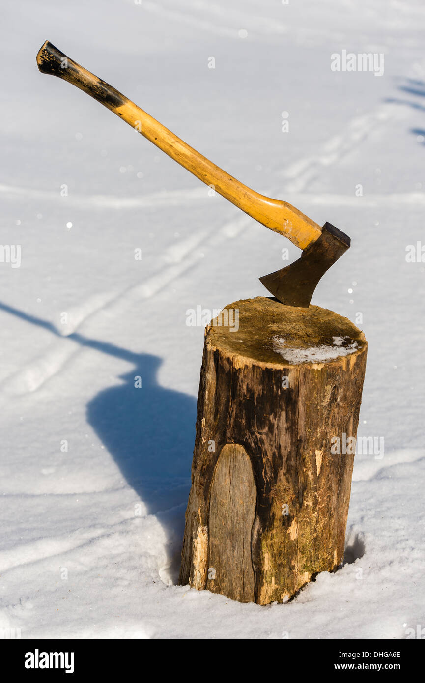 Ax stuck in wood log snow winter Stock Photo