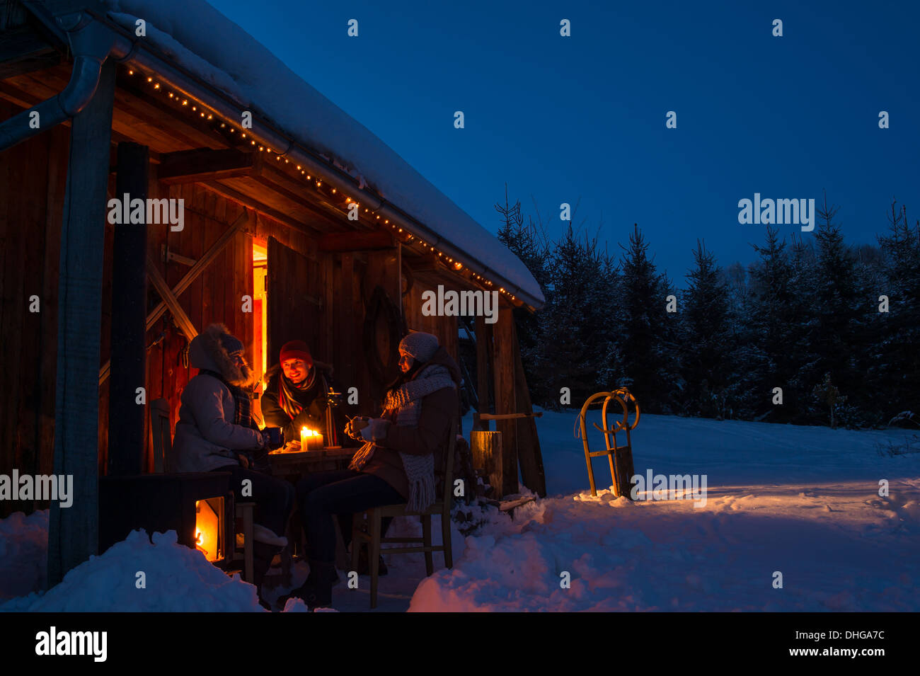 Evening winter cottage friends enjoy hot drinks in snow countryside Stock Photo