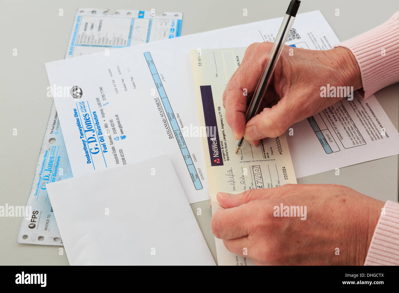 Senior woman pensioner writing a Nat West bank cheque to pay for a large oil fuel bill for home heating in Wales, UK, Britain Stock Photo